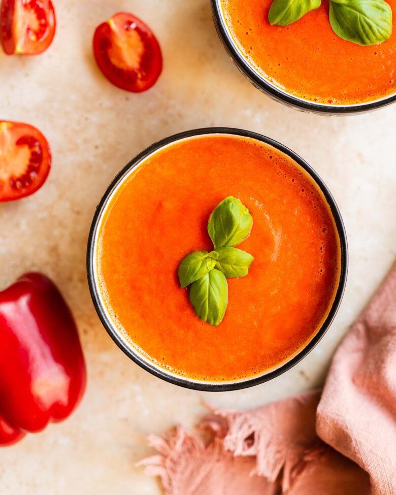 A bowl of creamy roasted red pepper and tomato soup, garnished with fresh basil leaves. Image by Jaz Kitchen