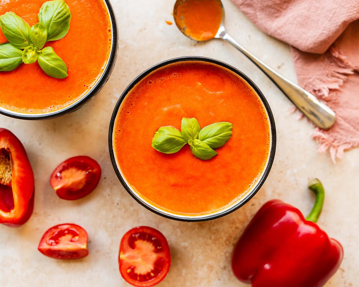 A bowl of creamy roasted red pepper and tomato soup, garnished with fresh basil leaves. Image by Jaz Kitchen